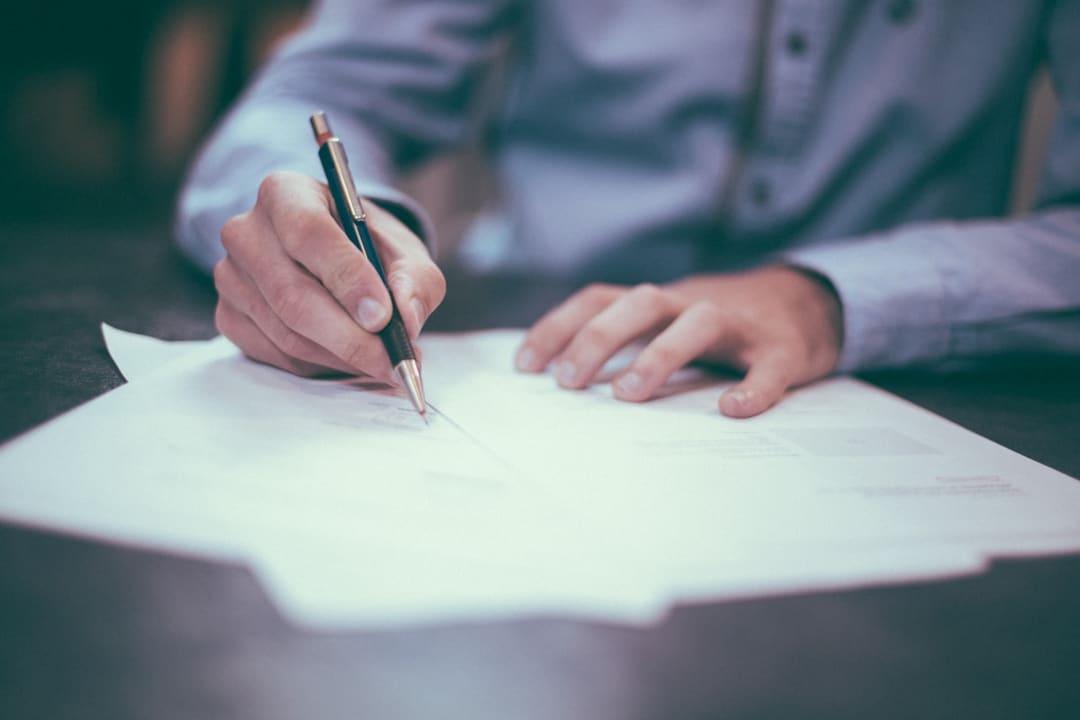 "Close-up of a hand signing an official document with a black pen on a wooden desk."